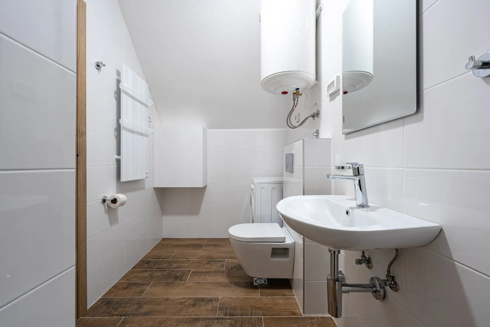 Manje kupatilo sa bijelim pločicama, umivaonikom i wc šoljom.