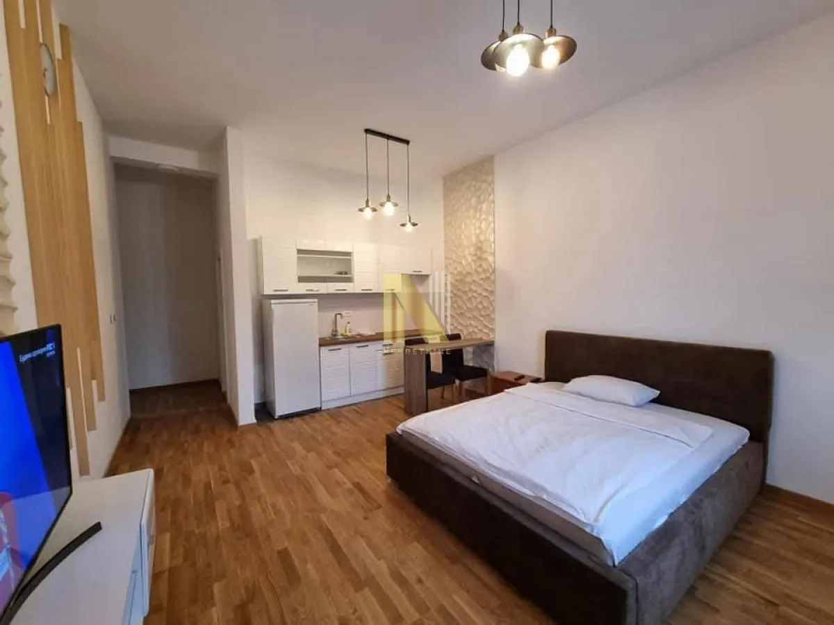 Garantovana spavaća soba sa bračnim krevetom i malom ugrađenom kuhinjom u pozadini.