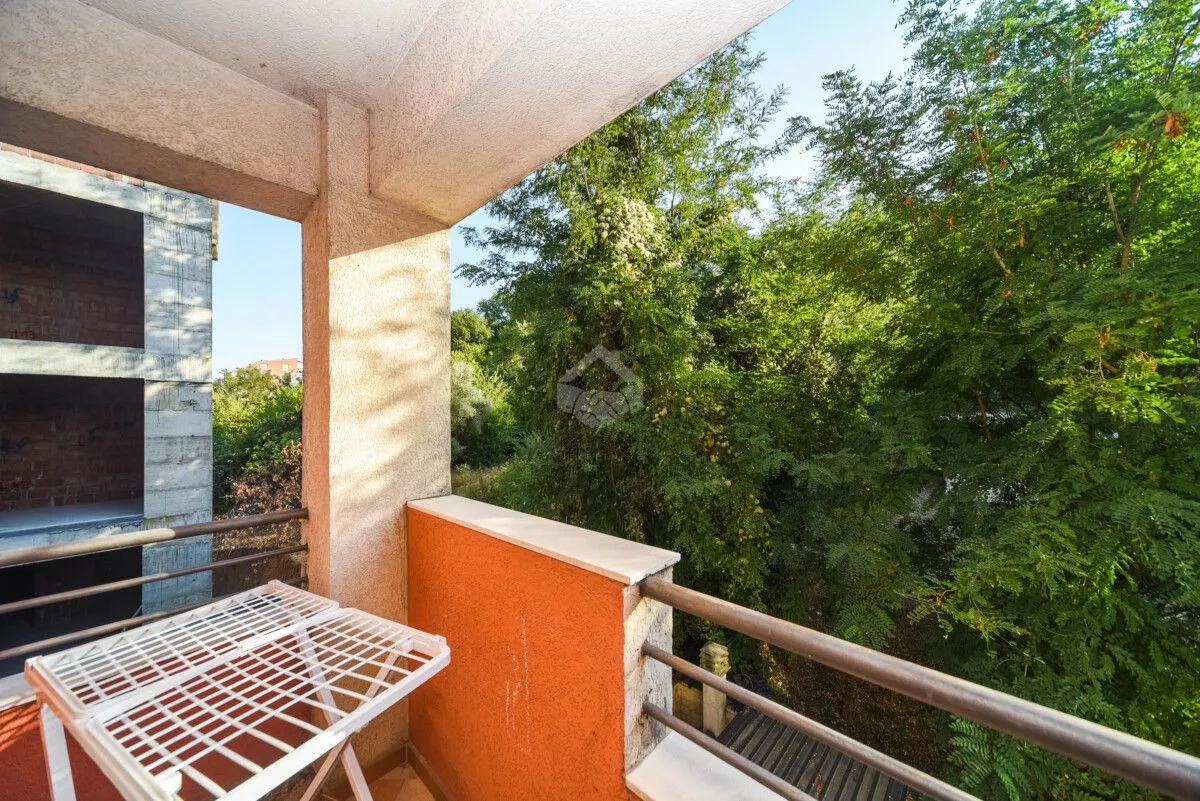 Natkriveni balkon sa pogledom na zeleno drveće.