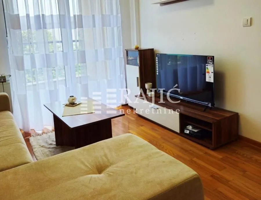 Living room with a sofa set, TV unit, and a large window.