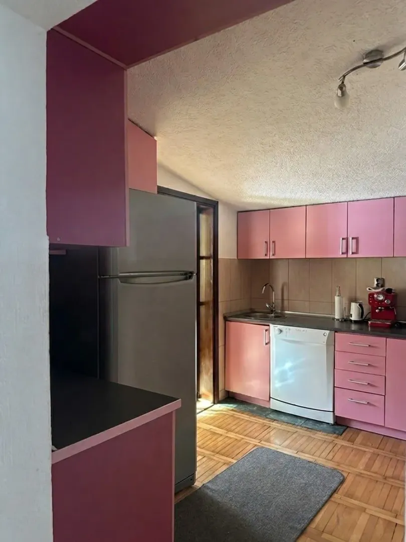Kuhinja sa roze elementima, frižiderom i drvenim podom.
