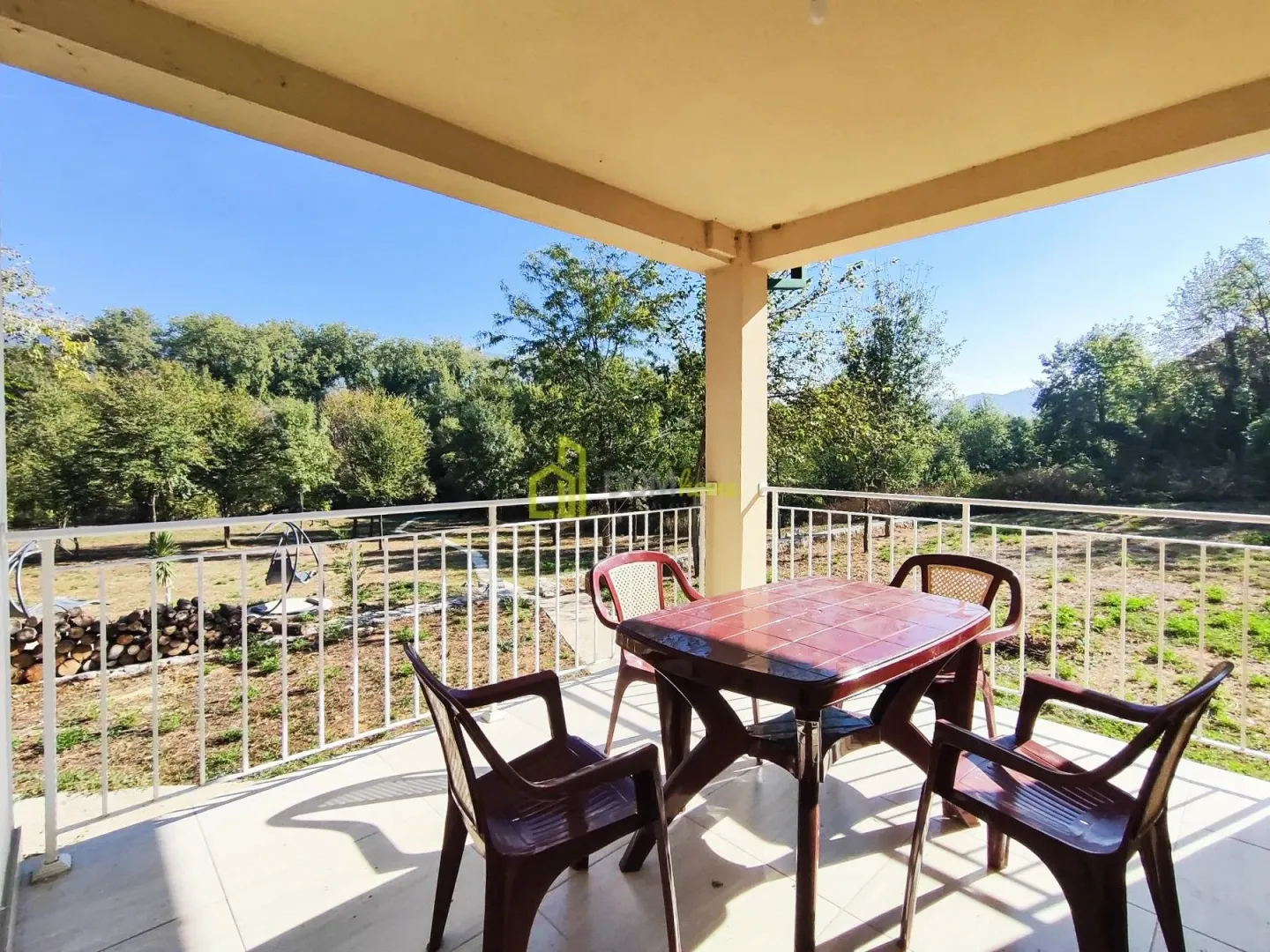 Covered terrace with a table and chairs and a view of the yard and nature.