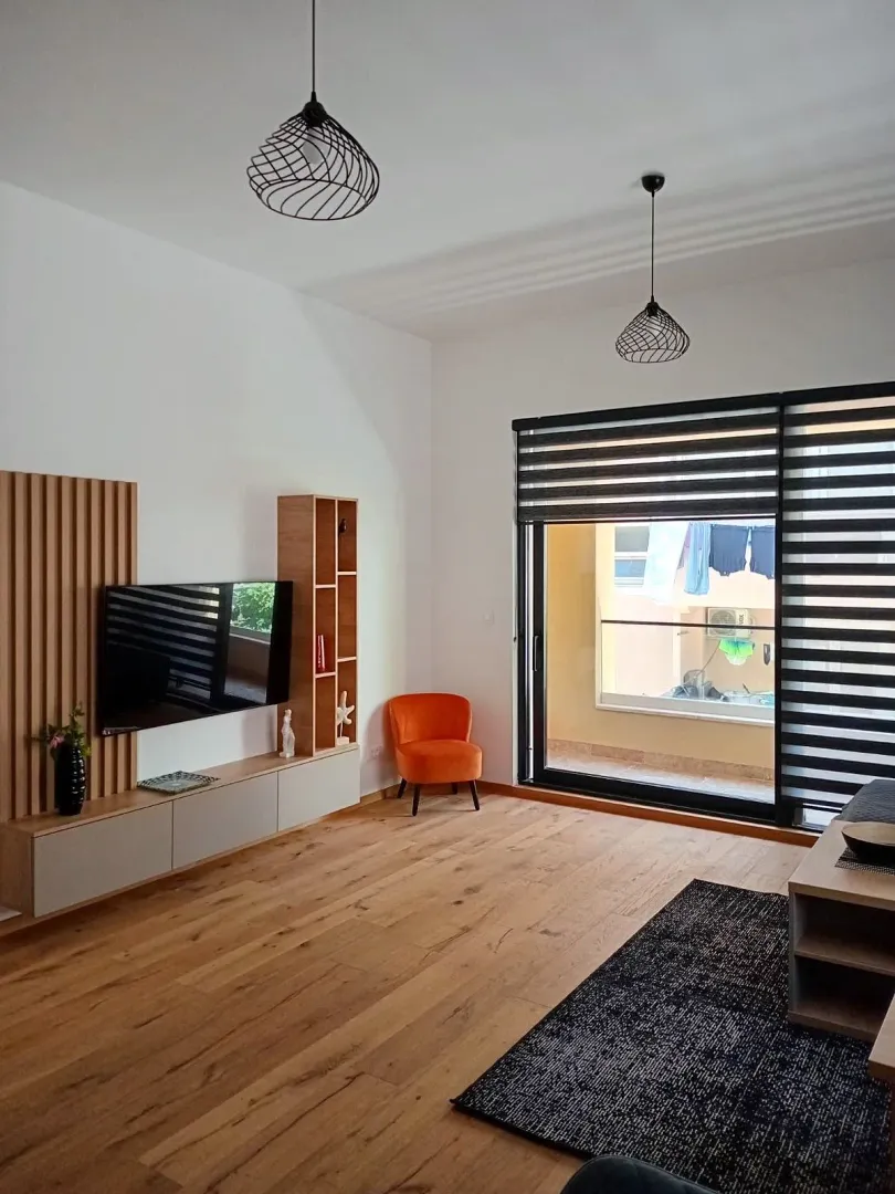 Spacious living room with wooden flooring, TV unit, and access to the terrace.