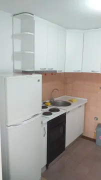 A small kitchen with white cabinets, a refrigerator, and a stove. - image 5