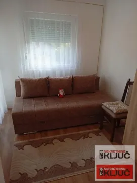 Manja dnevna soba sa braon trosedom, tepihom i prozorom sa zavesama. - image 5