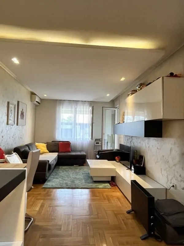 Living room with sofa, TV unit, and parquet flooring.