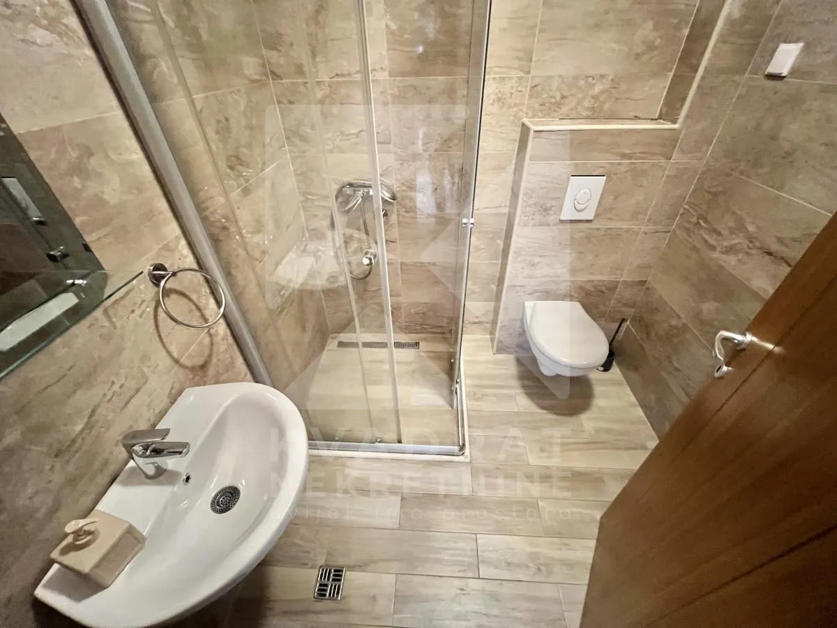 Small bathroom with a walk-in shower, washbasin, and wall-mounted toilet.