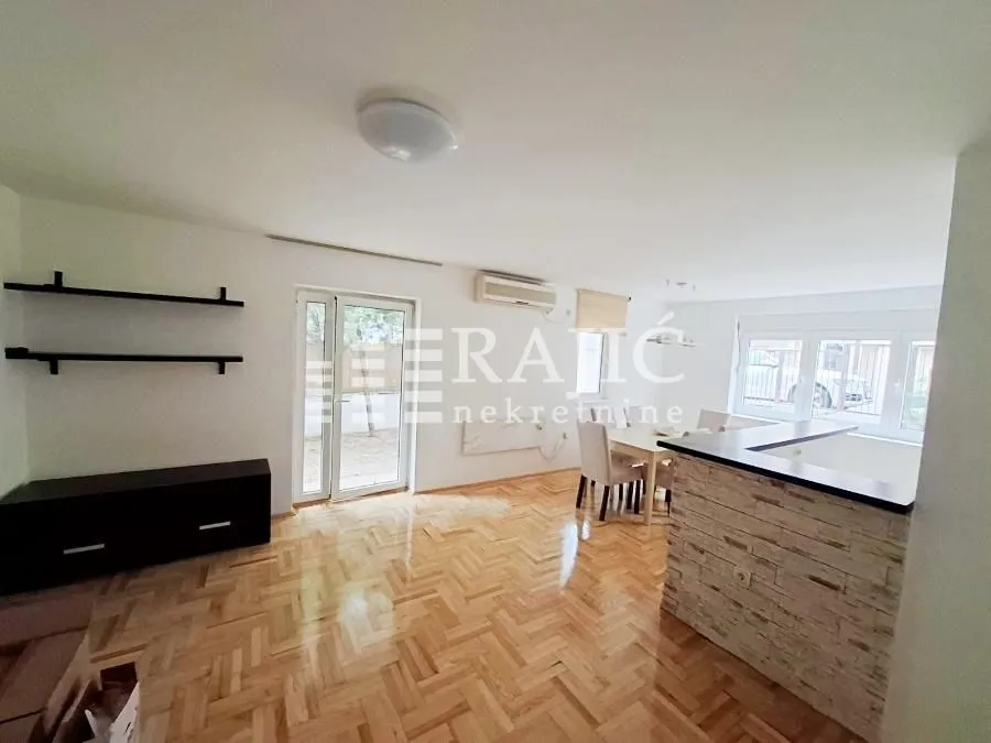 Spacious living room with parquet flooring and a dining area in the background.