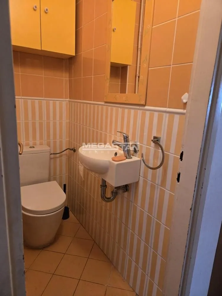 Manje kupatilo obloženo žutim pločicama sa WC šoljom i umivaonikom.