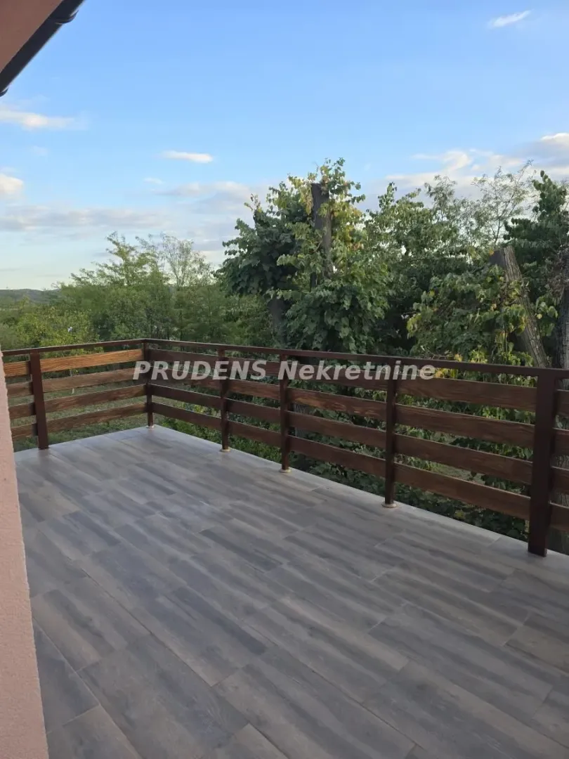 Spacious balcony with a wooden railing and a view of greenery.