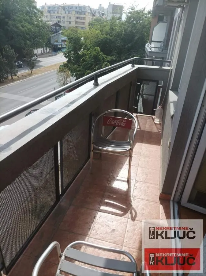 Uski popločani balkon sa metalnom ogradom i pogledom na ulicu.