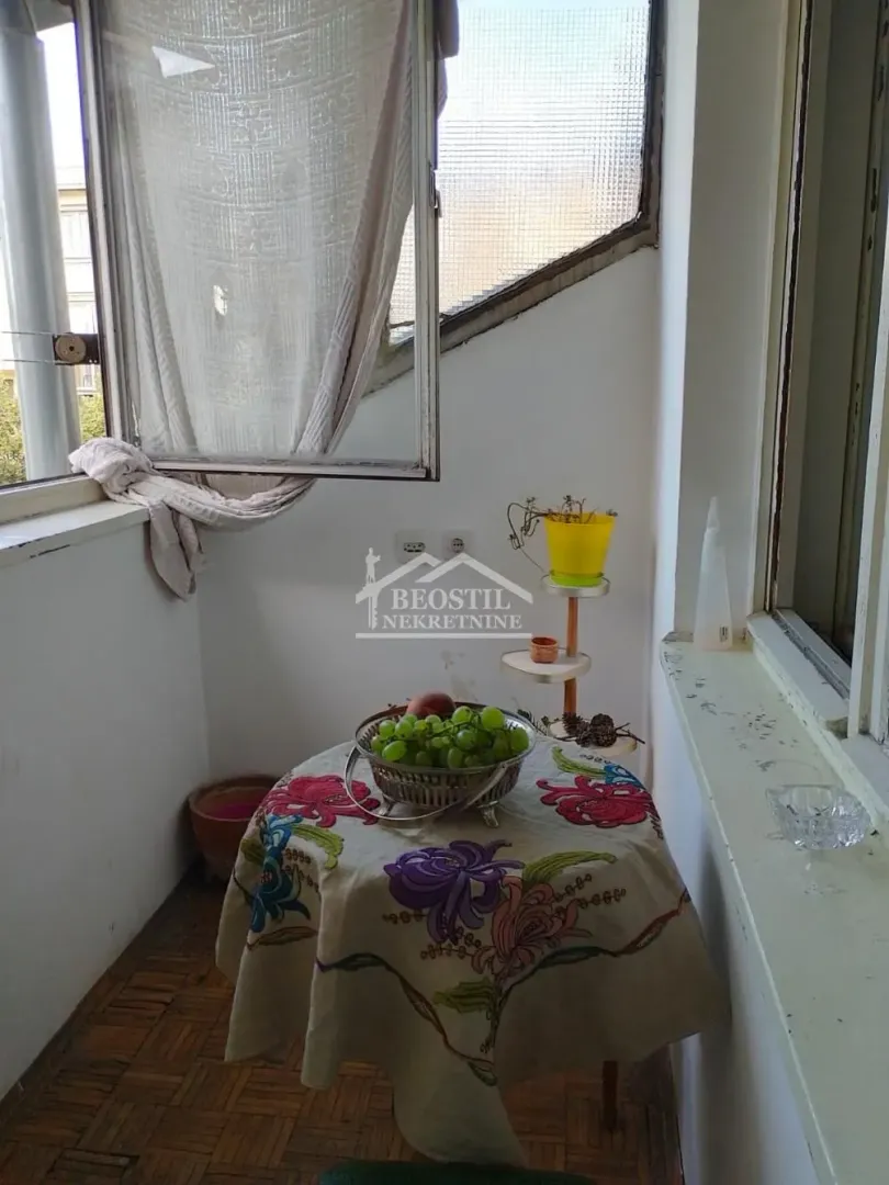 Manji zatvoreni balkon sa stolom prekrivenim stolnjakom i voćem.