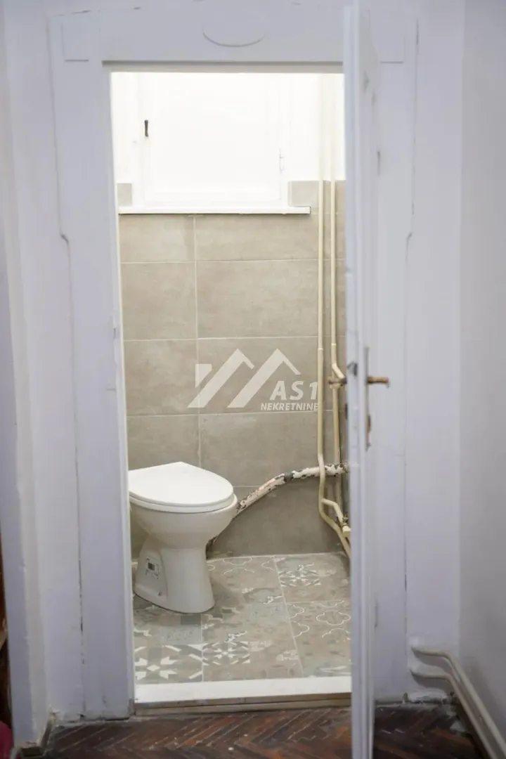 Pogled kroz vrata na kupatilo sa pločicama i wc šoljom.