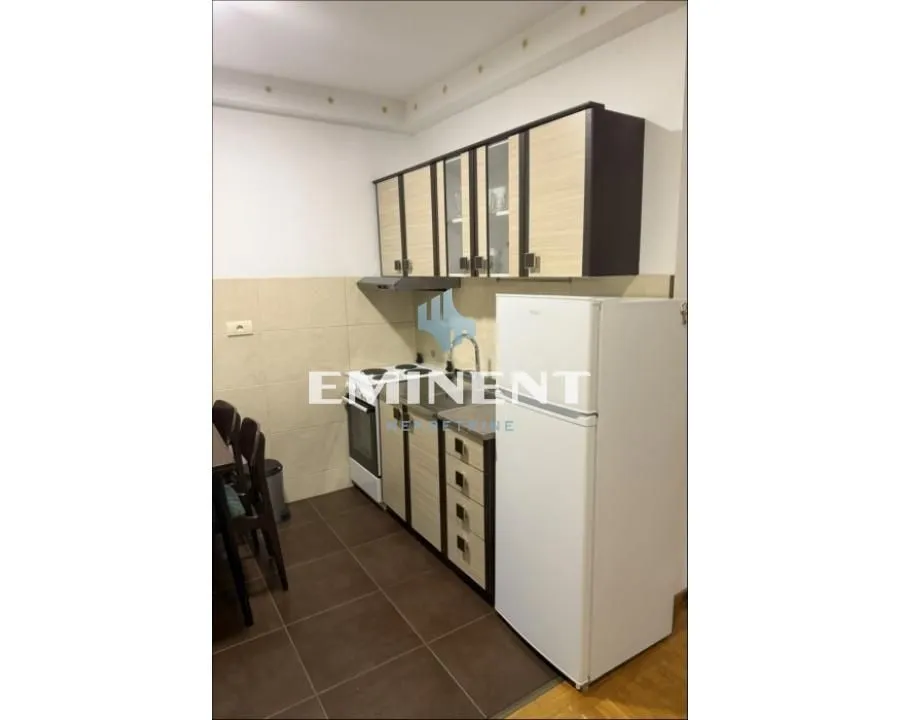 Manja kuhinja sa drvenim elementima i belim frižiderom.