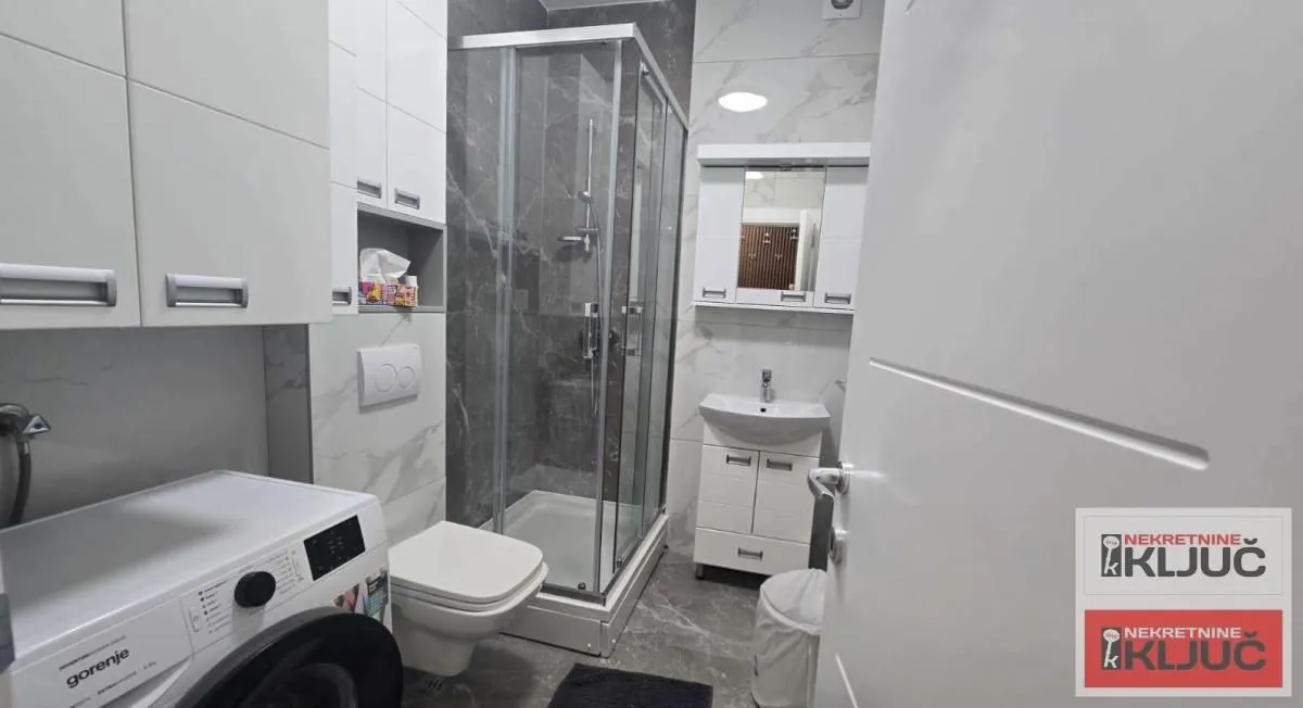 Modern bathroom with a shower cabin, washbasin, and washing machine.