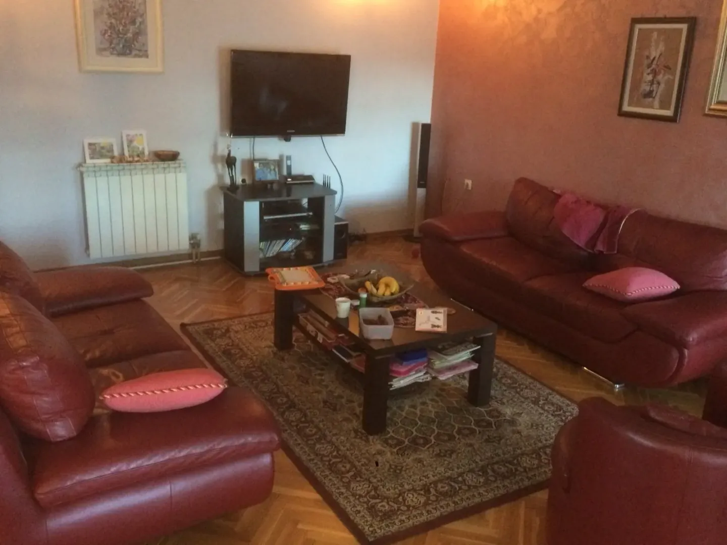 Dnevna soba sa crvenim kožnim garniturama i televizorom na zidu.
