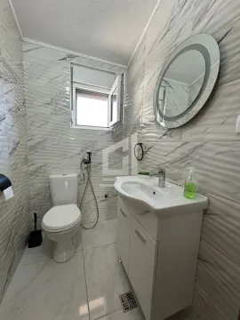 Smaller bathroom with white tiles, washbasin, toilet, and round mirror. - image 7