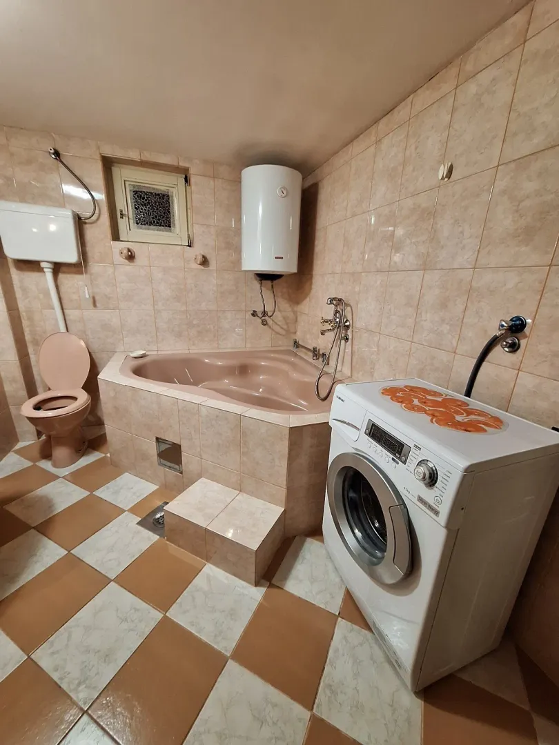 A bathroom with a large bathtub, washing machine, and beige tiles.