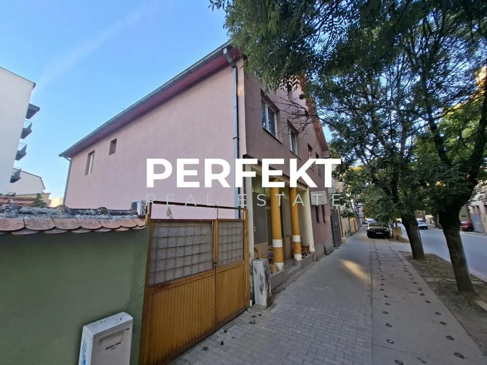 Pogled na spoljašnjost kuće sa dvorišnom kapijom i trotoarom.