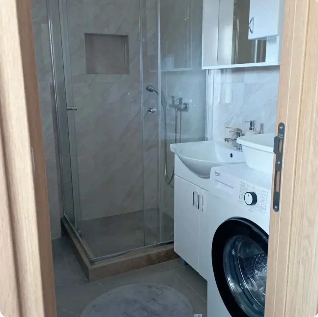 Moderne kupatilo sa tuš kabinom, umivaonikom i veš mašinom.