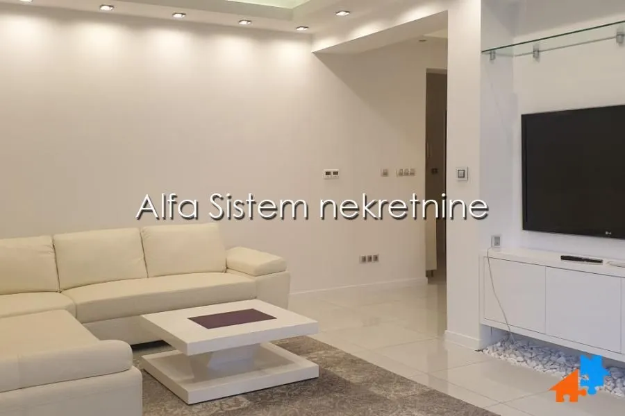 Living room with a white sectional sofa, coffee table, and wall-mounted TV.