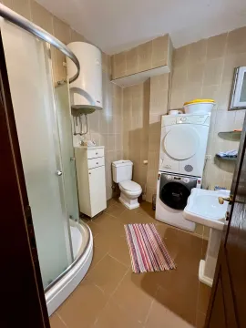 Fully equipped bathroom with a shower cabin, toilet, sink, and washing machine. - image 9