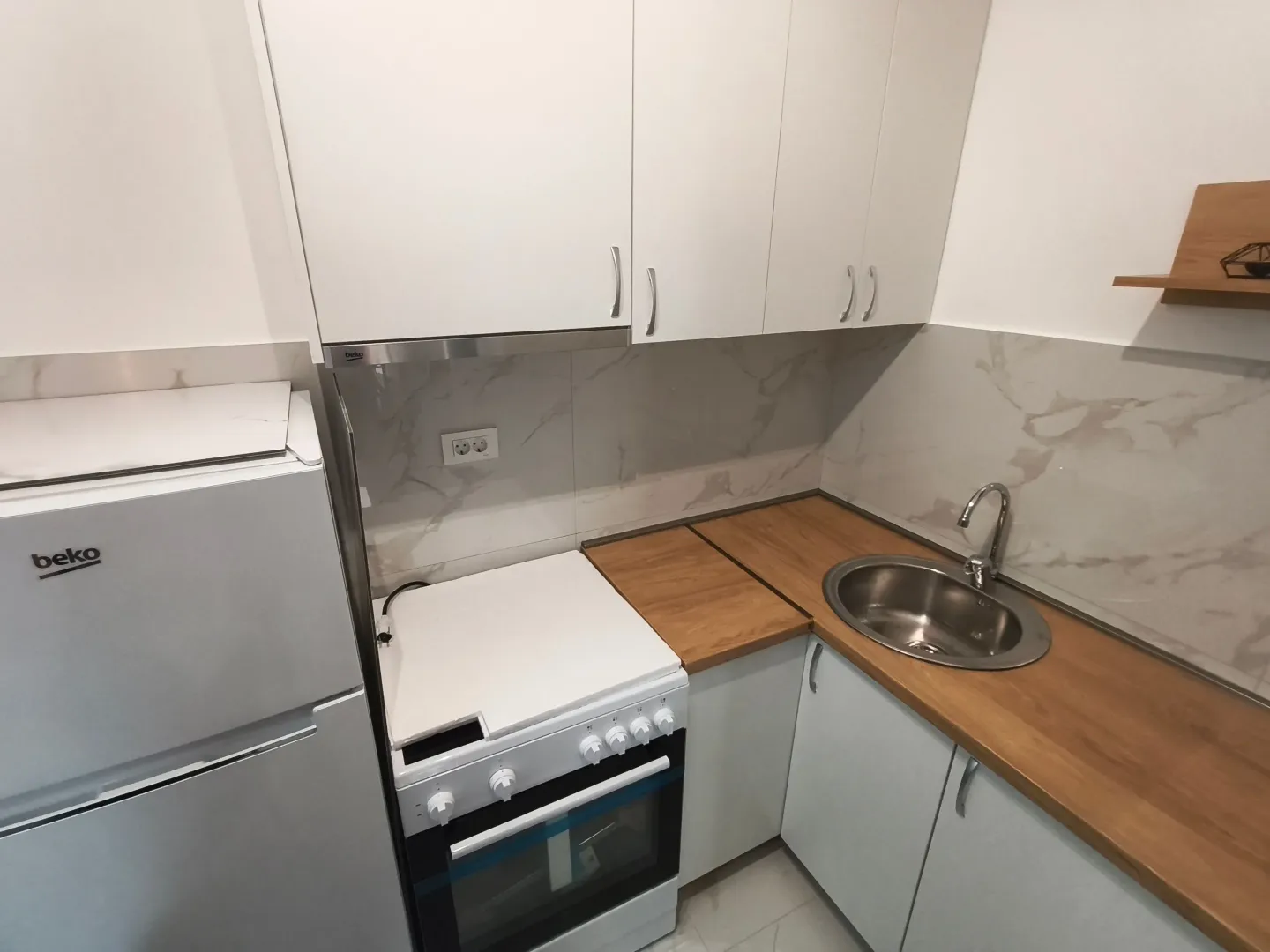 Compact kitchen with white cabinetry, a stove, and a sink.