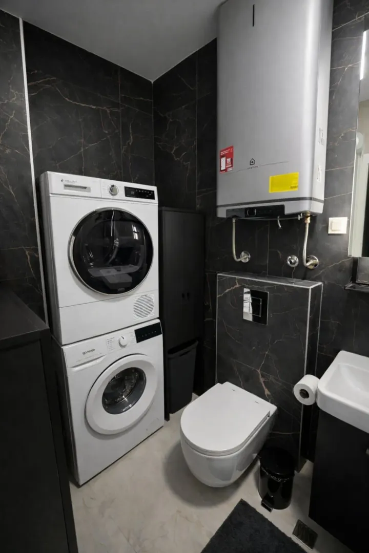 Modern bathroom with dark tiles, washing machine, and dryer.
