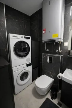 Modern bathroom with dark tiles, washing machine, and dryer. - image 12