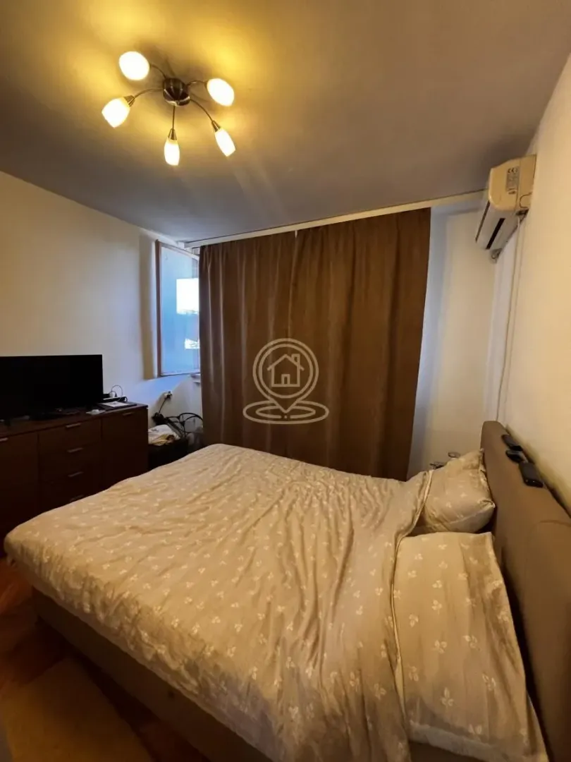 Nameštena spavaća soba sa bračnim krevetom, komodom i klima uređajem.