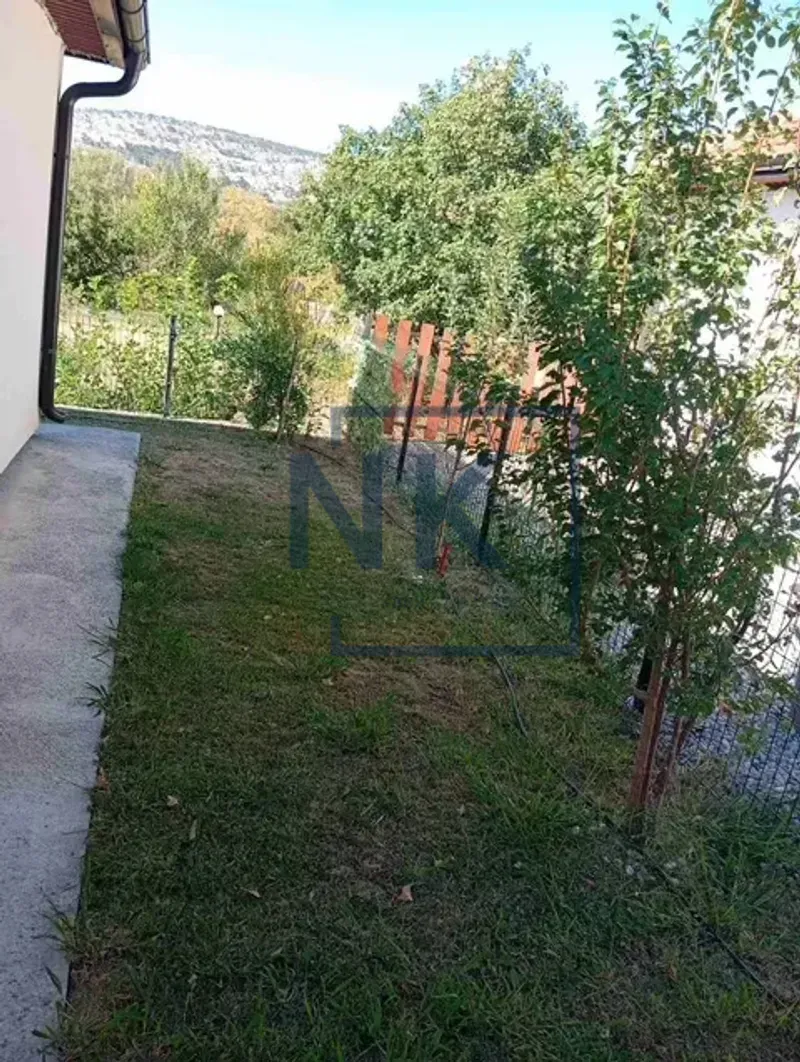 Green yard next to the house with a fence and trees.
