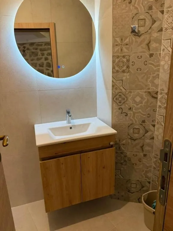 Bathroom with a vanity unit, sink, and a round backlit mirror.