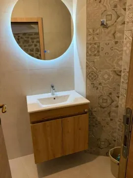 Bathroom with a vanity unit, sink, and a round backlit mirror. - image 14
