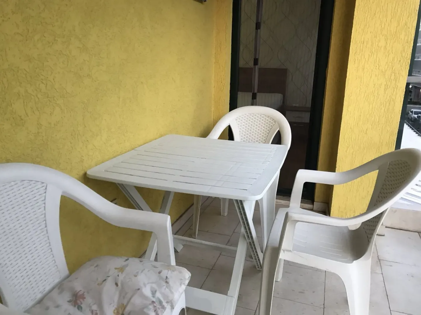 Balcony with a white plastic table and chairs next to a yellow wall.