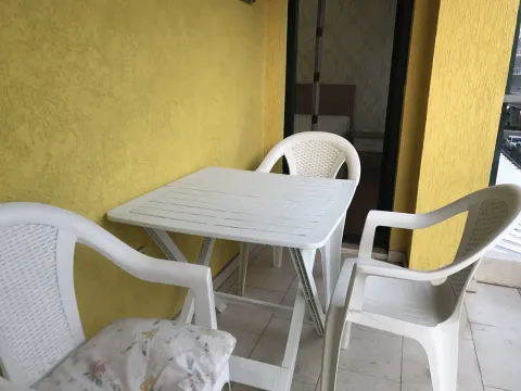 Balcony with a white plastic table and chairs next to a yellow wall. - image 10