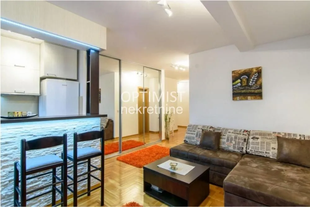 Living room with a sectional sofa, coffee table, and a bar counter separating the kitchen area.