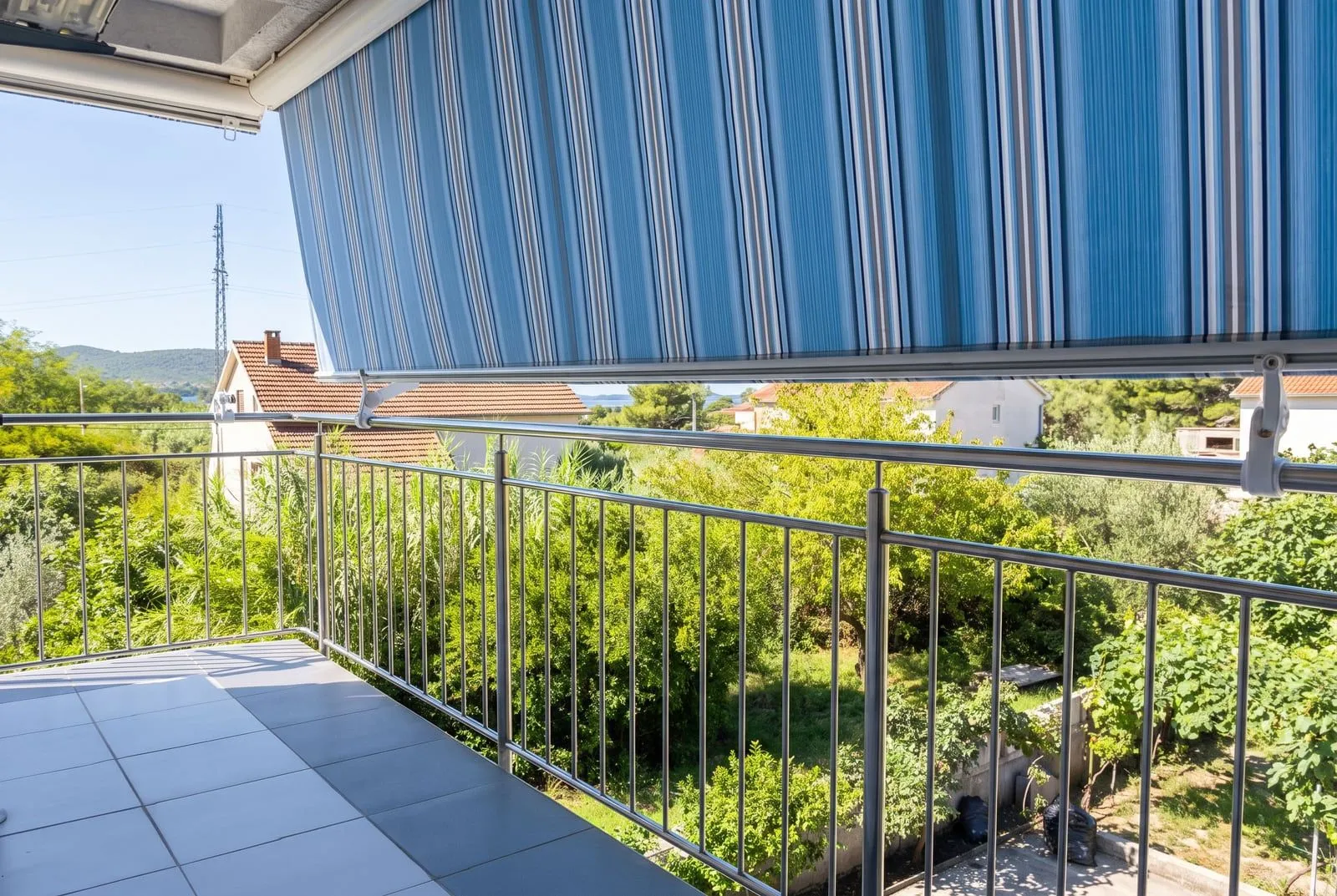 Natkriveni balkon sa metalnom ogradom i pogledom na prirodu i kućice.
