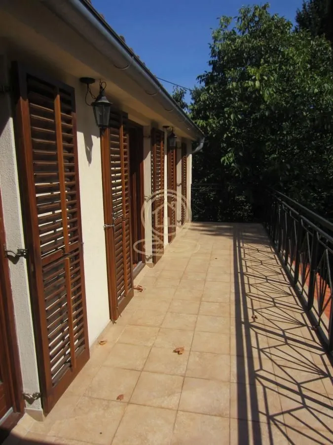 Spacious tiled terrace with wooden shutters and a view of greenery.