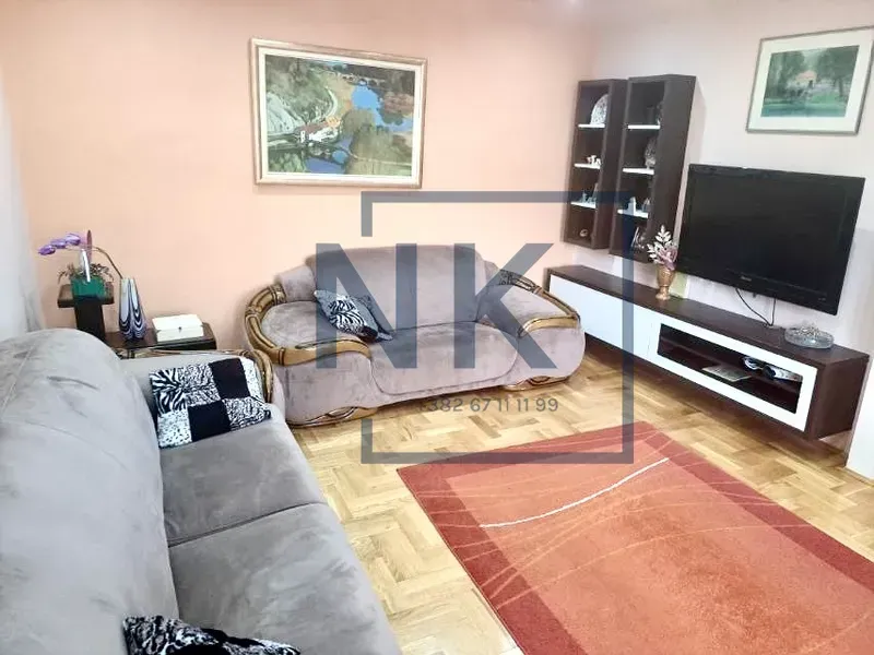 Dnevna soba sa garniturom, televizorom i parketom na podu.