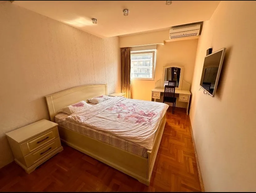 Spavaća soba sa velikim bračnim krevetom, radnim stolom i televizorom na zidu.