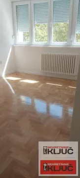 Prazna soba sa parketom, belim zidovima i prozorima sa roletnama. - image 6