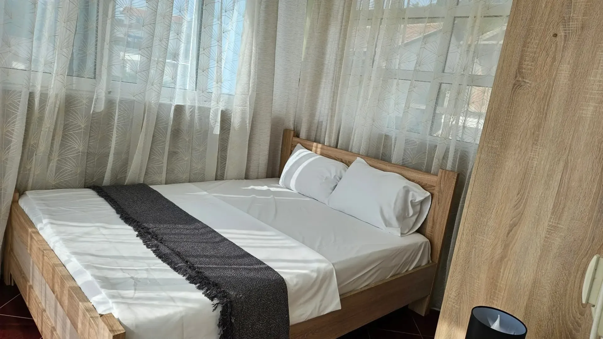 Bright bedroom with a wooden bed and curtain-covered windows.