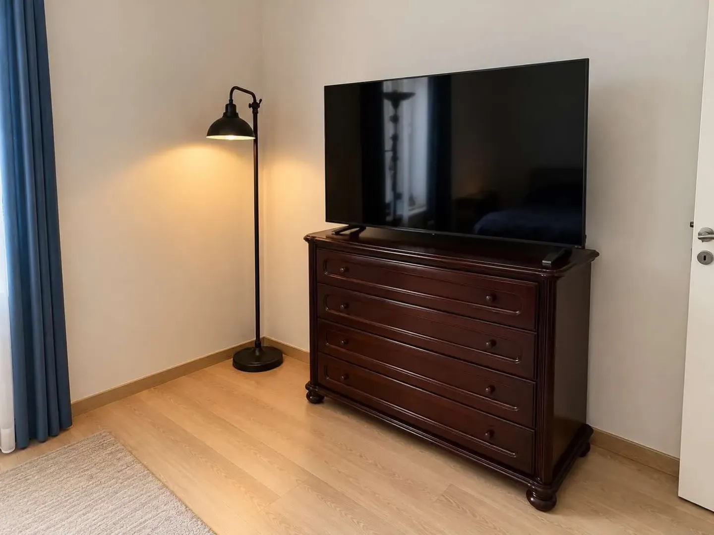 Spavaća soba sa komodom, televizorom i podnom lampom.