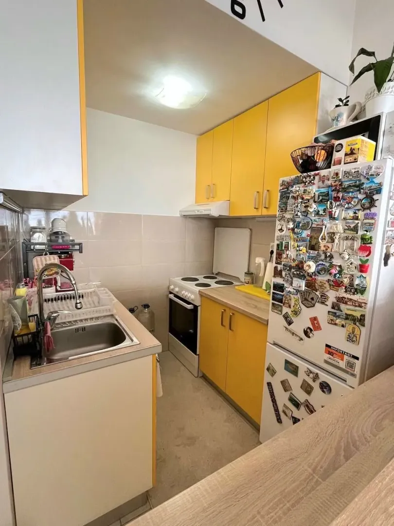 Manja kuhinja sa žutim elementima i bijelim frižiderom prekrivenim magnetima.