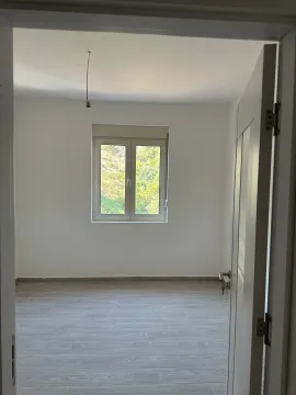 Prazna soba sa bijelim zidovima i prozorom kroz koji se vidi zelenilo. - image 9