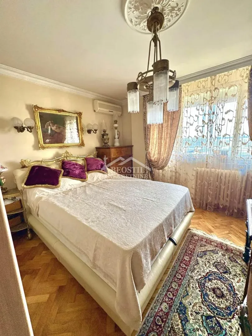 Prostrana spavaća soba sa bračnim krevetom, lusterom i tepihom.