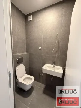 Manje kupatilo obloženo sivim pločicama sa toaletom i umivaonikom. - image 8