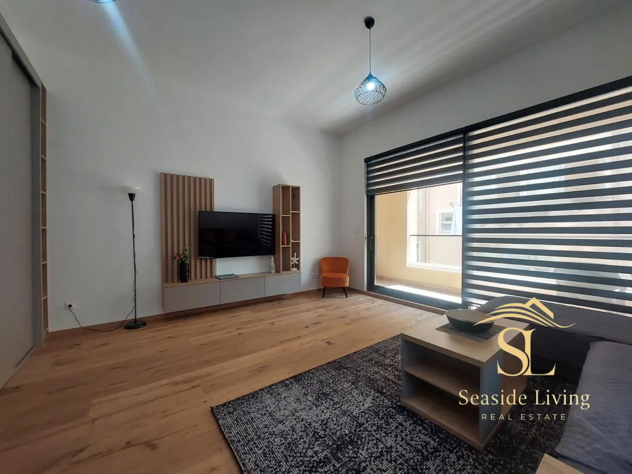 Modern living room with wooden flooring, TV unit, and access to the terrace.
