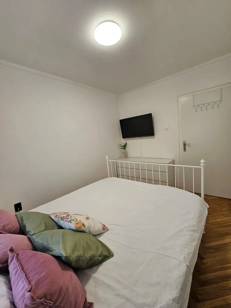 Uredna spavaća soba sa bijelim krevetom i komodom.