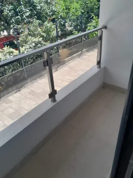 An empty balcony with a glass railing and a view of a paved path and greenery. - image 4